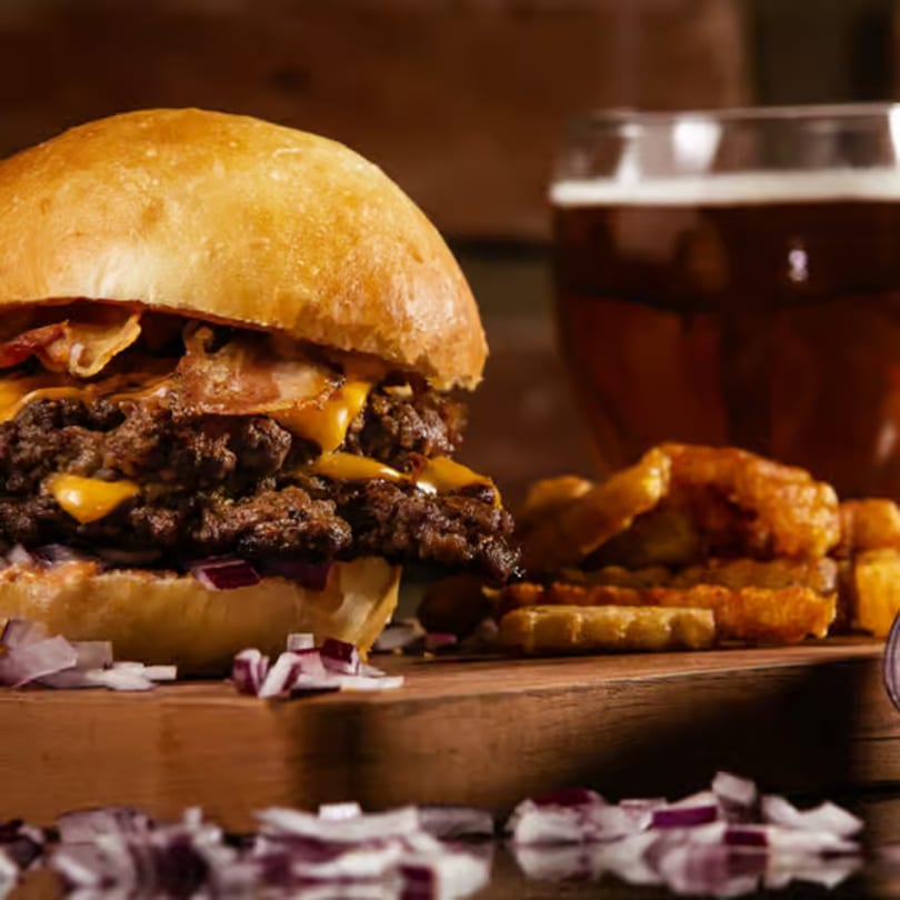 Double cheeseburger with bacon, fries, and a glass of beer on a wooden board.