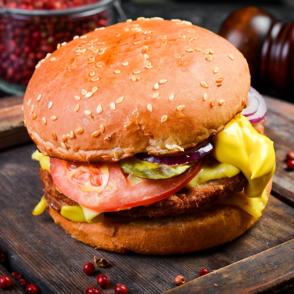 A close-up of a burger with a sesame seed bun, tomato, onion, pickles, and mustard.