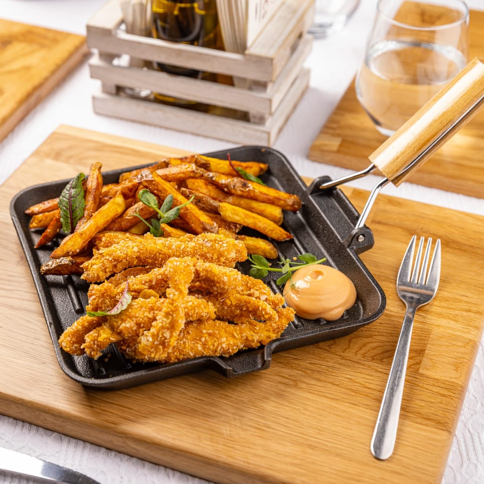 Crispy chicken tenders and sweet potato fries with dipping sauce on a black skillet.